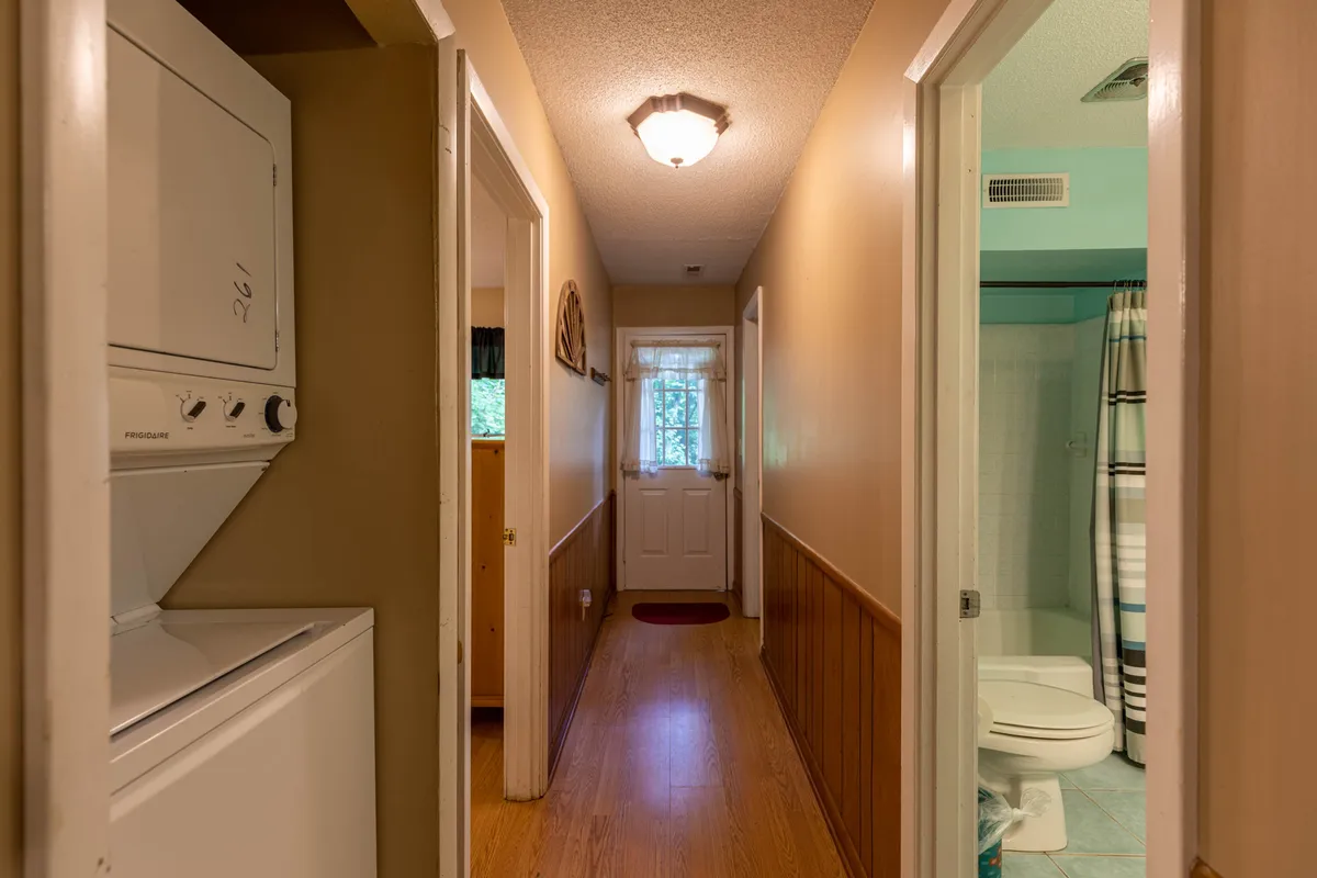 This image showcases a functional interior space featuring a laundry unit, bathroom and front door, all highlighted against natural wood paneling. The atmosphere is homey and practical, with visible evidence of cleanliness (laundry area) and order (organized entryway) that suggests a well-maintained environment.