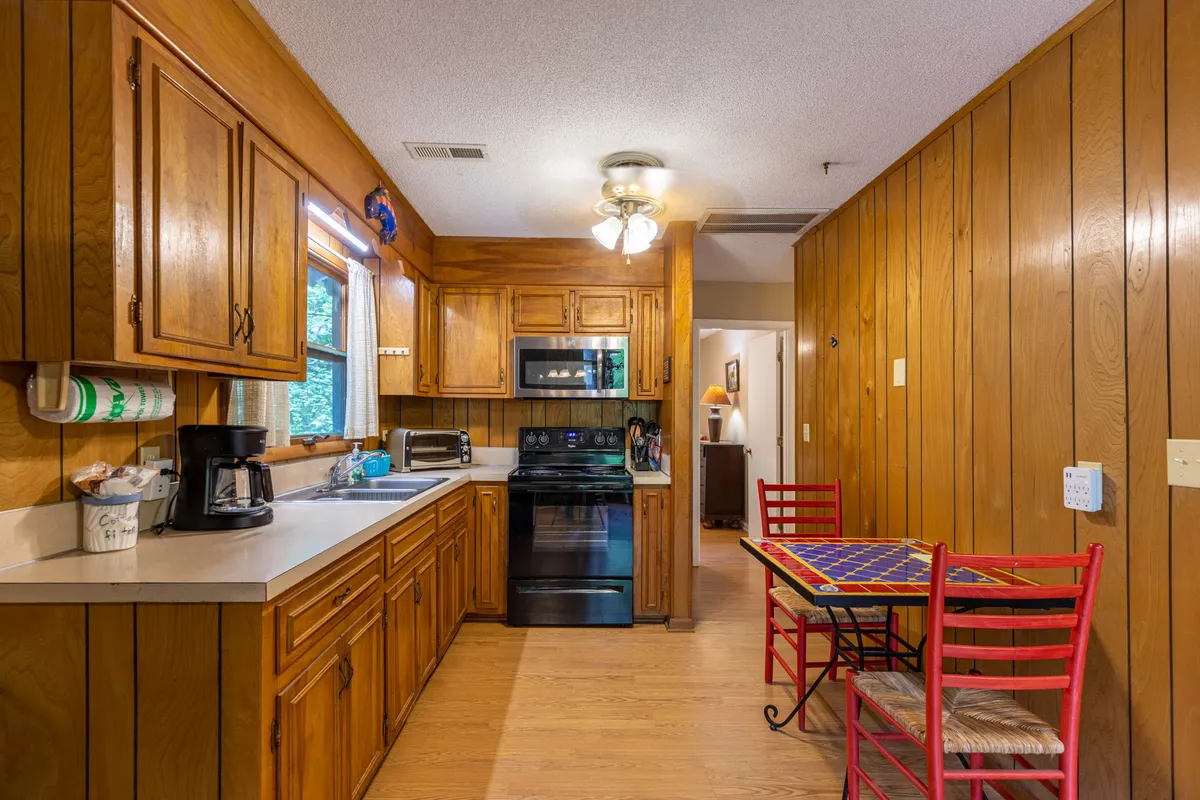 A welcoming kitchen and dining area featuring kitchen cabinets, sleek black appliances, vibrant red chairs, and a table with a colorful tablecloth. The space is set for cooking, casual meals, and family gatherings, echoing the cabin's spirit of togetherness.